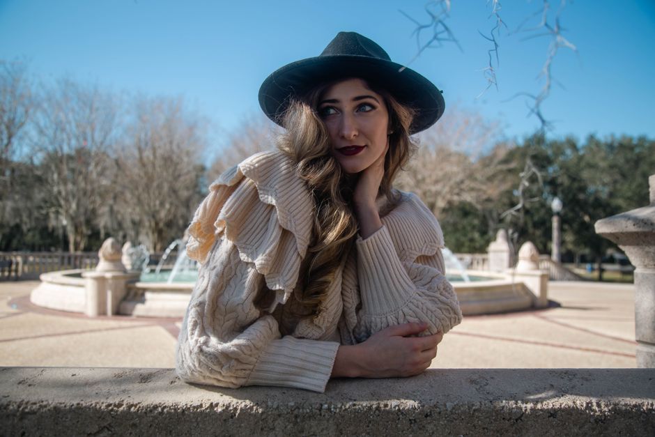 Woman wearing a cream ribbed sweater with ruffled shoulders styled for fall