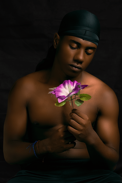 Free A topless man poses with a vibrant flower against a black backdrop, focusing on serenity and reflection. Stock Photo