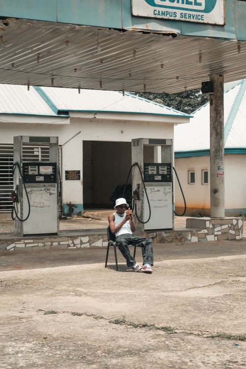 dapper man pumping gas while smoking cigarette Man Smoking Cigarette at Gas Station · Free Stock Photo