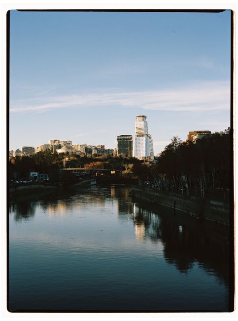 Scenic view of Tbilisi cityscape featuring a river and skyline under a clear blue sky.