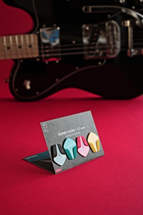 Free Stylish guitar picks in various colors displayed with a sleek black electric guitar on a red backdrop. Stock Photo