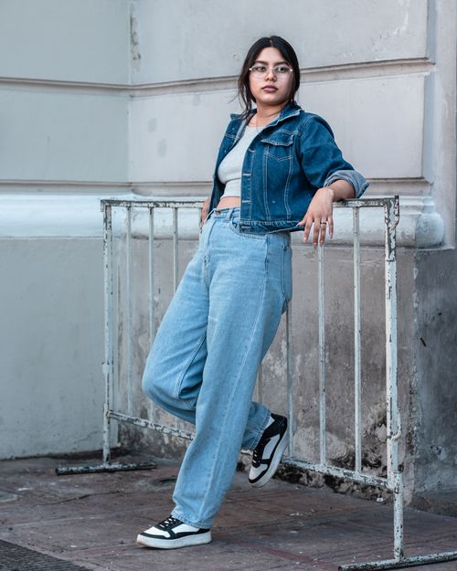 Free Stylish woman wearing denim jacket and jeans posing against an outdoor wall. Stock Photo