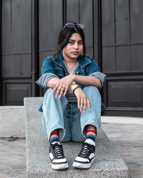 Free Stylish woman sitting in denim jacket and jeans, posing confidently outdoors. Stock Photo