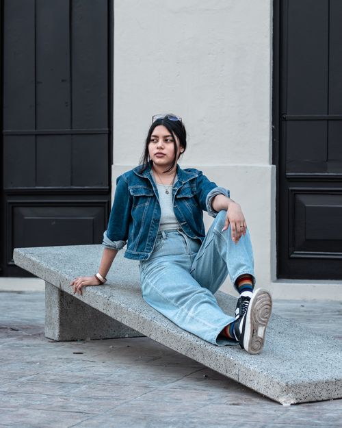 Free Young woman in denim jacket and jeans sitting on an urban bench in a casual fashion pose. Stock Photo