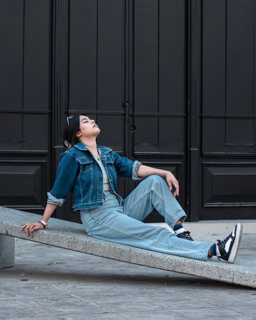 Free Fashionable woman in denim outfit sits relaxed on an urban bench, showcasing modern street style. Stock Photo