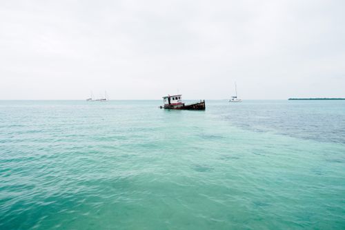 Free A peaceful seascape featuring an old shipwreck and yachts against a serene horizon. Stock Photo