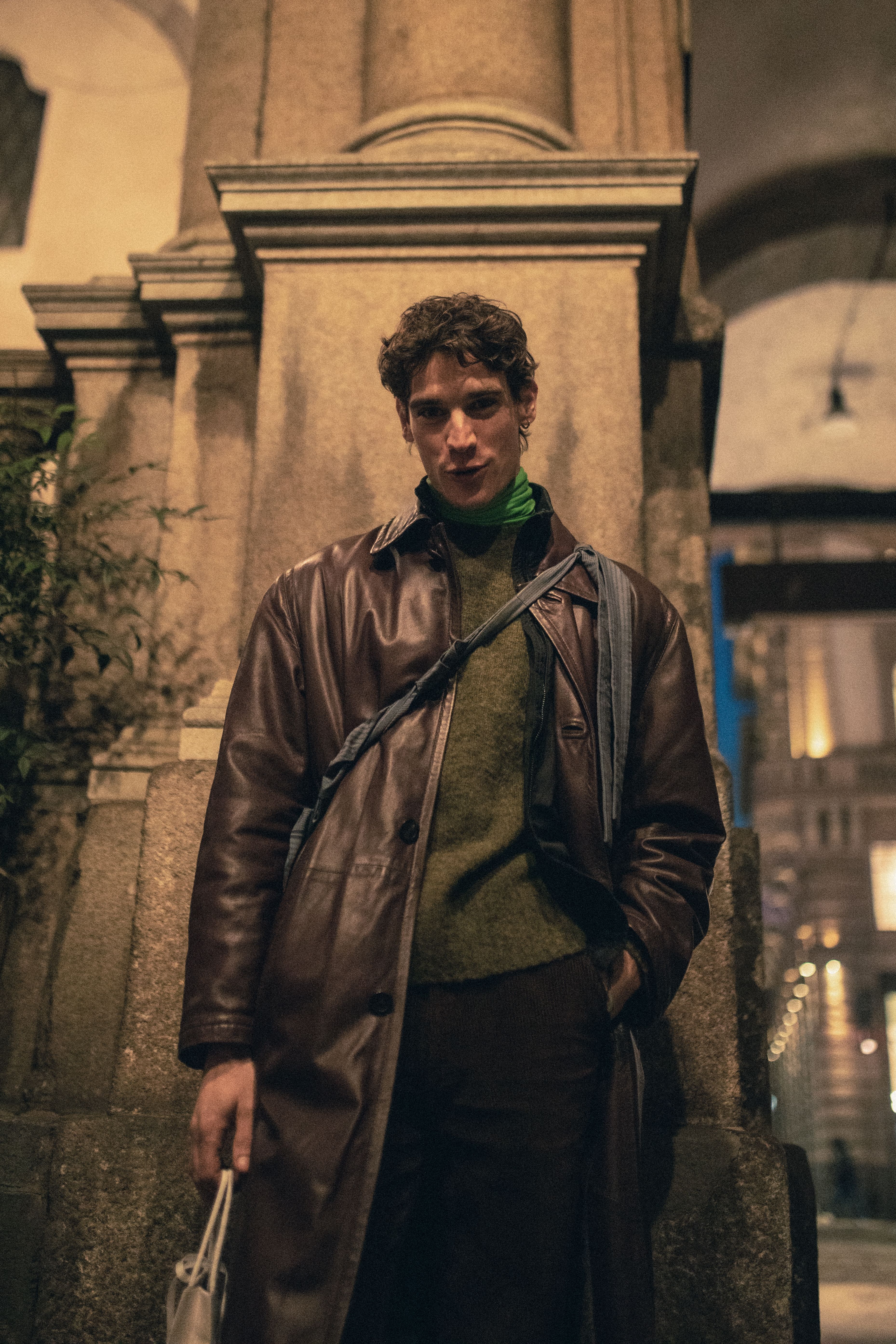 Stylish man in brown leather coat poses in Milan street at night.