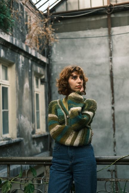Thoughtful woman in striped sweater poses in rustic urban setting.