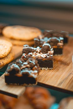 Close-up of chocolate brownies with icing on a wooden board, surrounded by cookies.