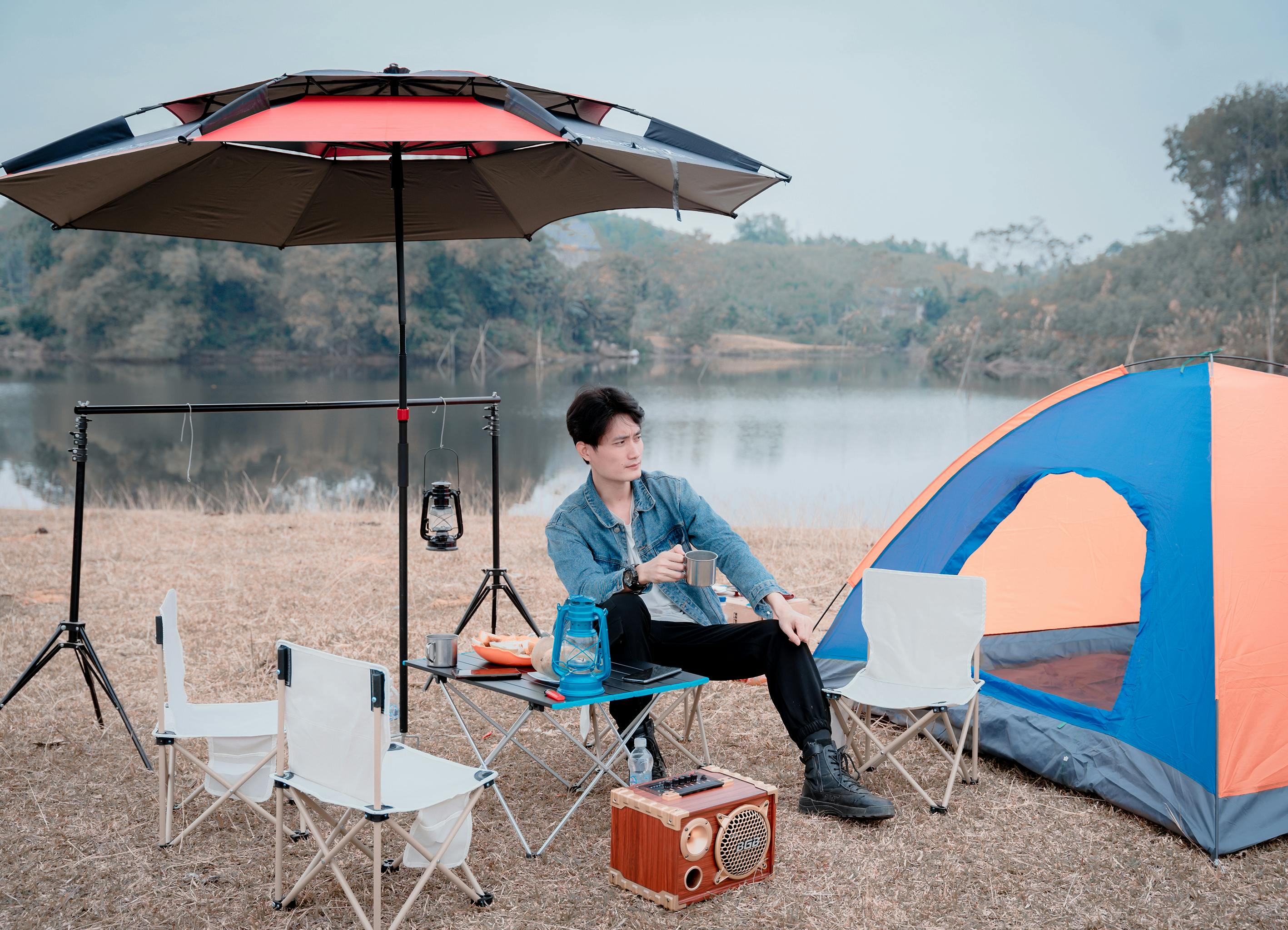A man enjoying a peaceful camping vacation by a lake with tent and camping gear.