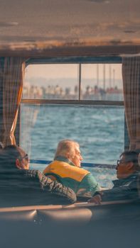 Three elderly men enjoying a scenic ferry ride through a window with water views.