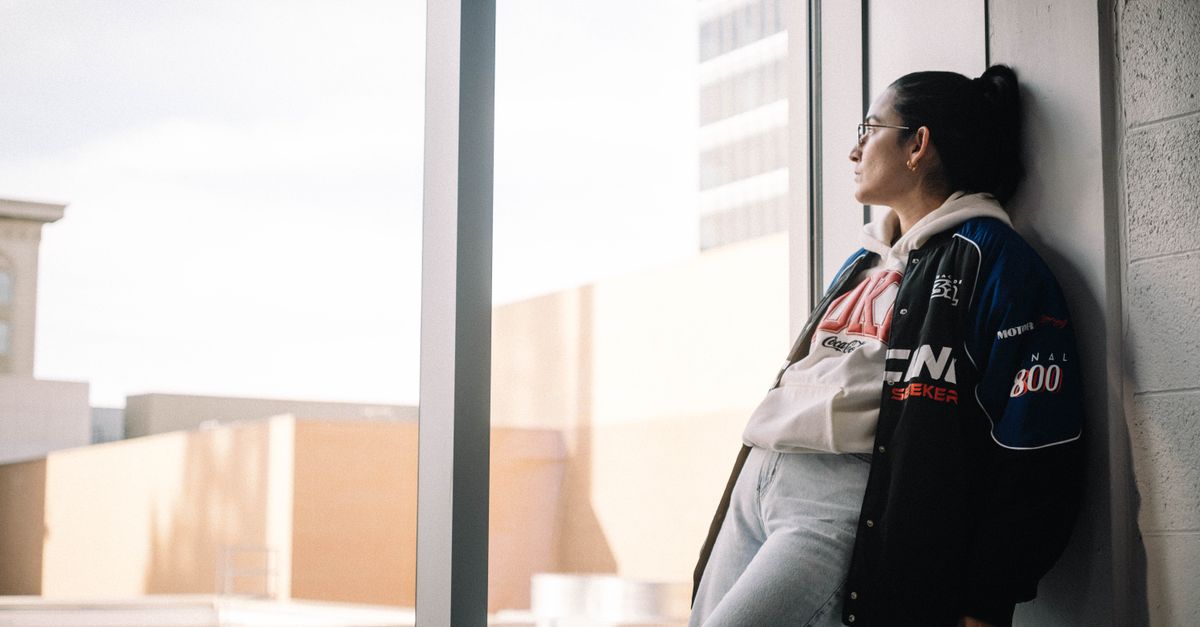 Young woman in urban attire gazing out of a modern building window.