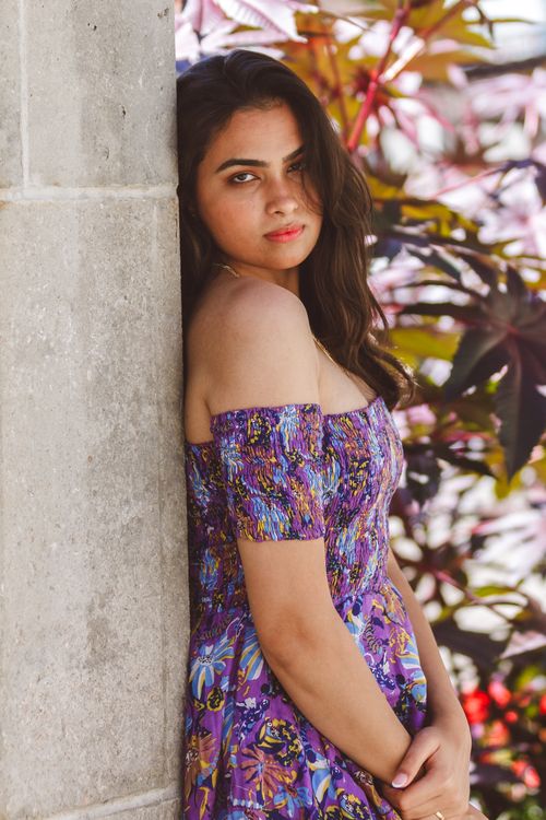 Free A woman with long brunette hair posing against a stone wall in a floral dress with a summer backdrop. Stock Photo