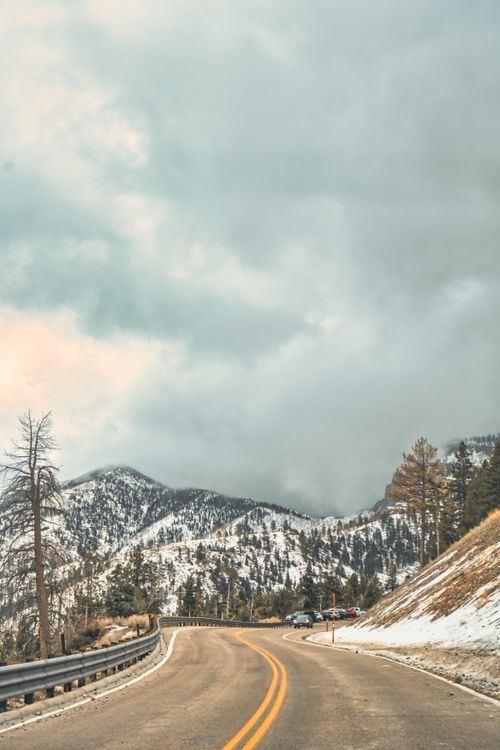 Free A winding road through snowy mountains under a dramatic overcast sky. Perfect for travel and adventure themes. Stock Photo