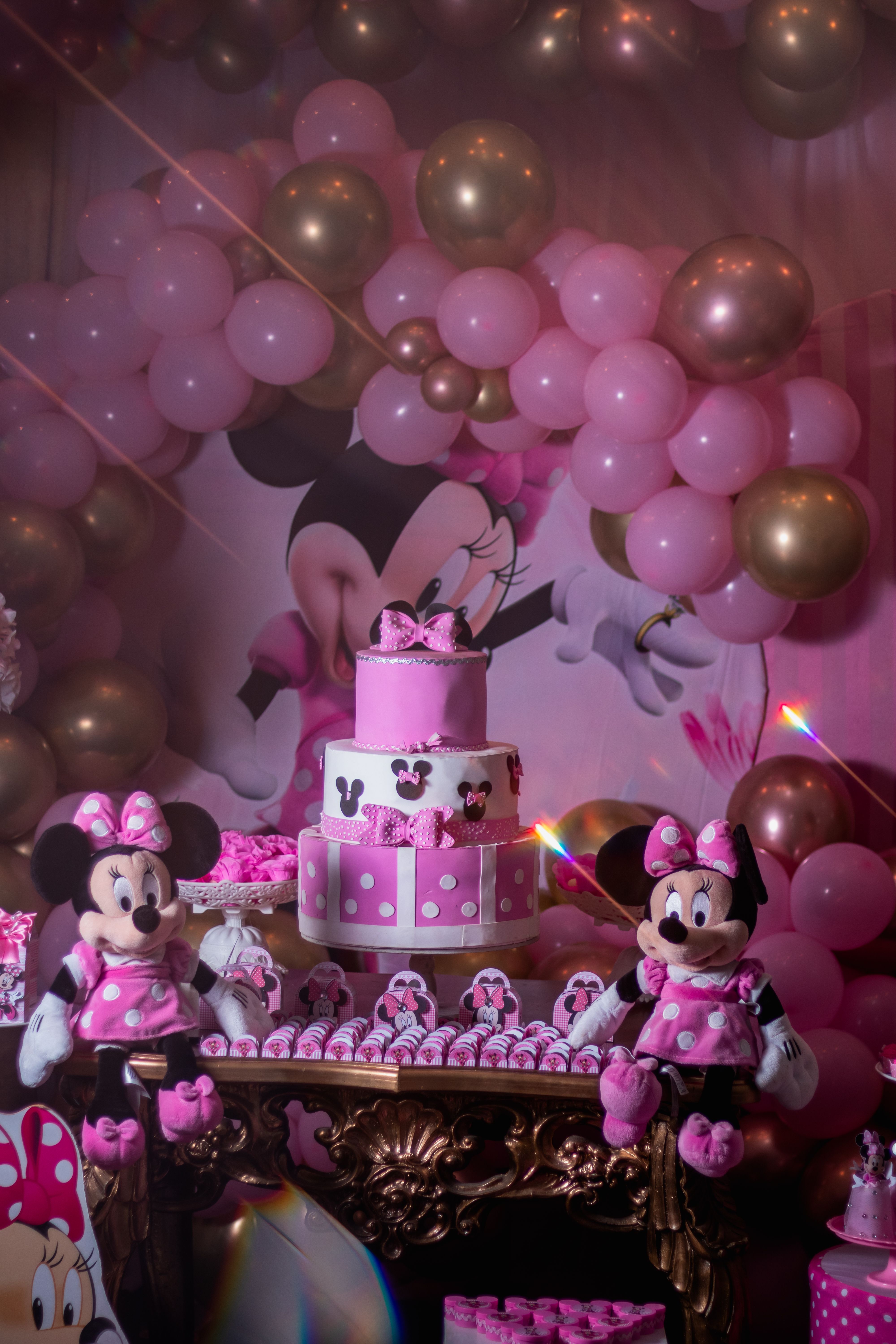 Festive Minnie Mouse themed party table with pink cake and balloons.