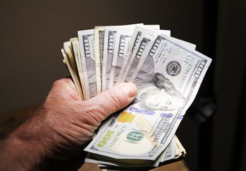 Close-up of a hand holding multiple hundred dollar bills on a dark background.