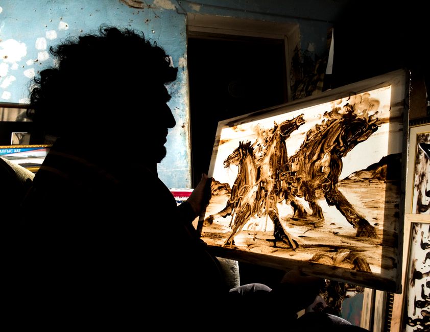 Silhouette of an artist holding a detailed painting of horses, captured indoors with dynamic light contrast.