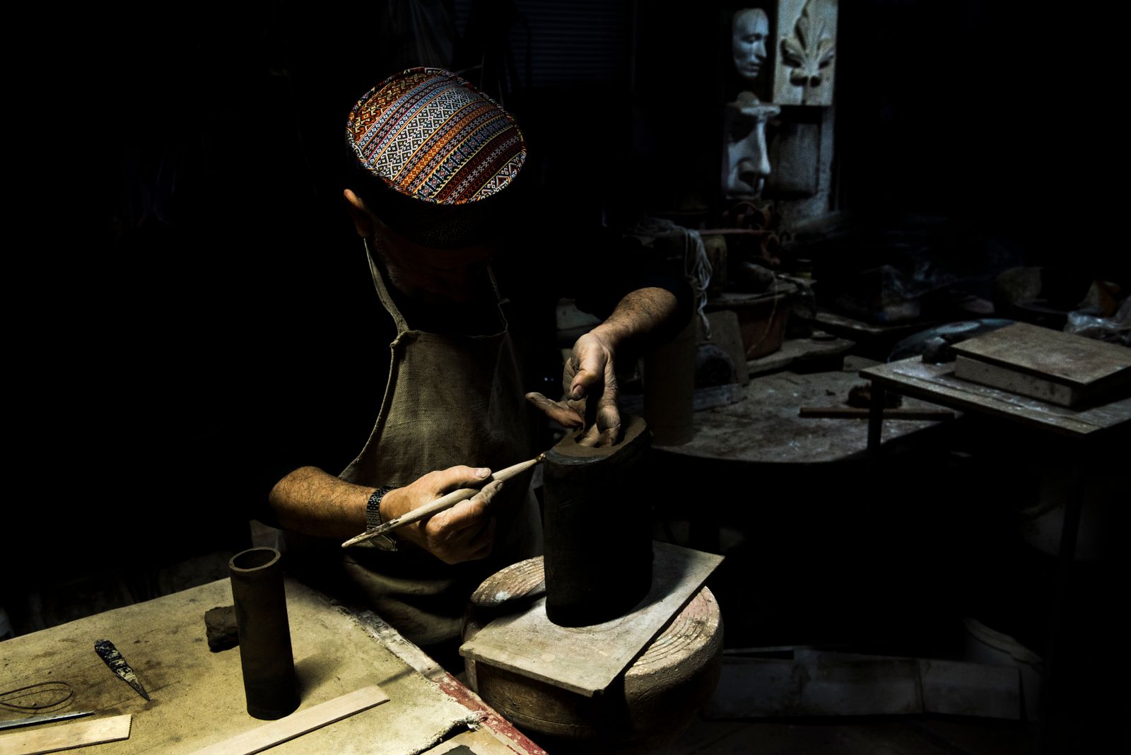 A maker shaping clay at a lamplit workbench in a low-lit studio. Photo by Elkhan Ganiyev on Pexels