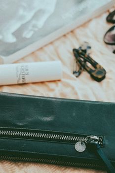 Stylish composition featuring a zipped leather handbag with sunglasses and cosmetics on a blanket.