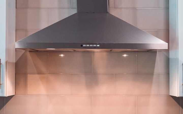 A contemporary kitchen scene featuring a stainless steel exhaust hood and a pot on the stove.