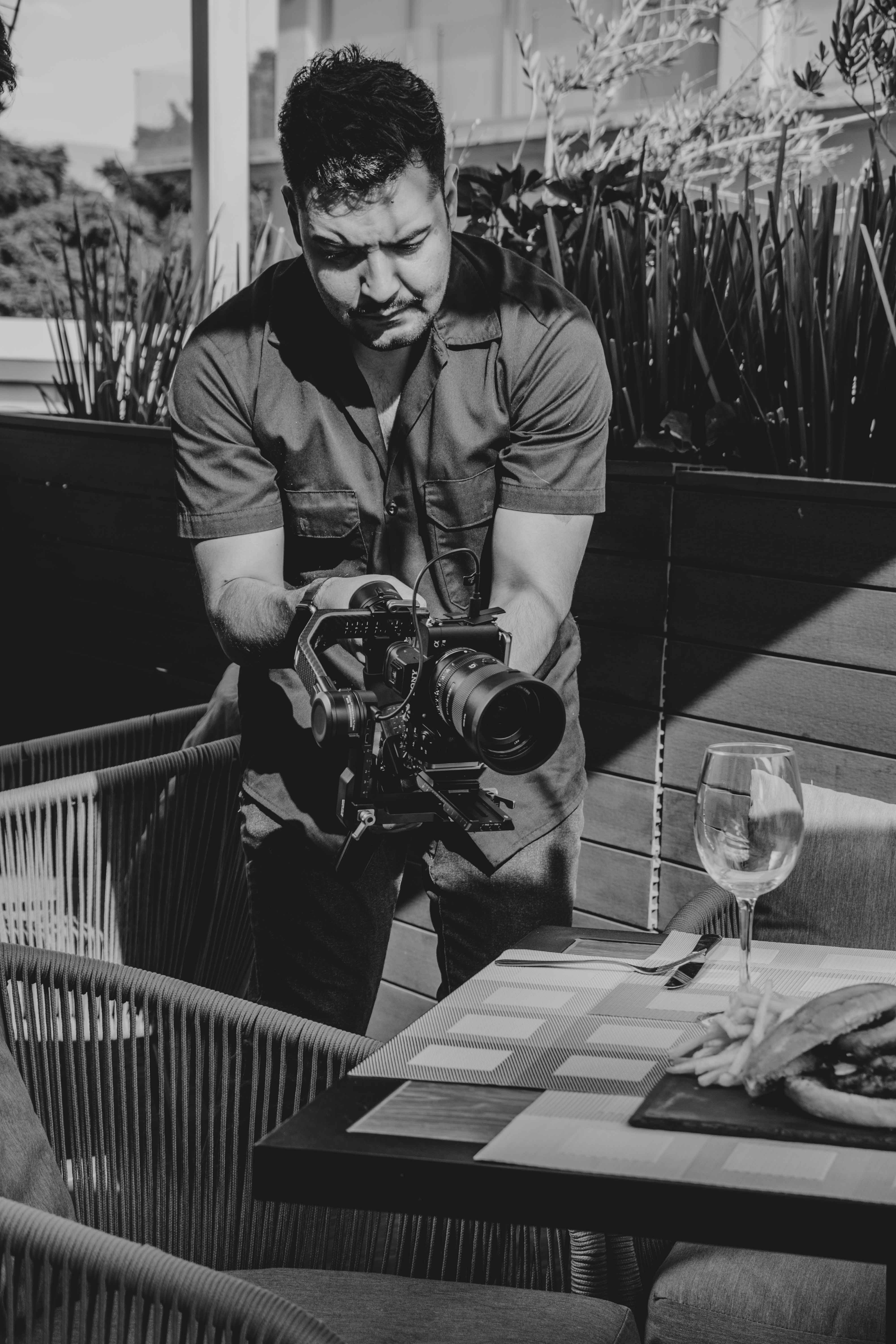 A cameraman captures footage in an outdoor restaurant scene, focusing on a table setting.