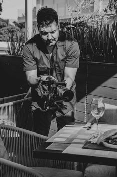 A cameraman captures footage in an outdoor restaurant scene, focusing on a table setting.