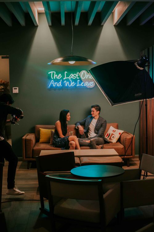 Free A couple being filmed in a cozy studio with moody lighting and a neon sign. Stock Photo