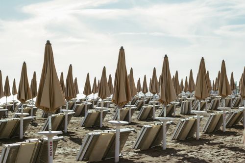 Free Peaceful scene of closed beach umbrellas aligned on sandy shore in Italy. Stock Photo