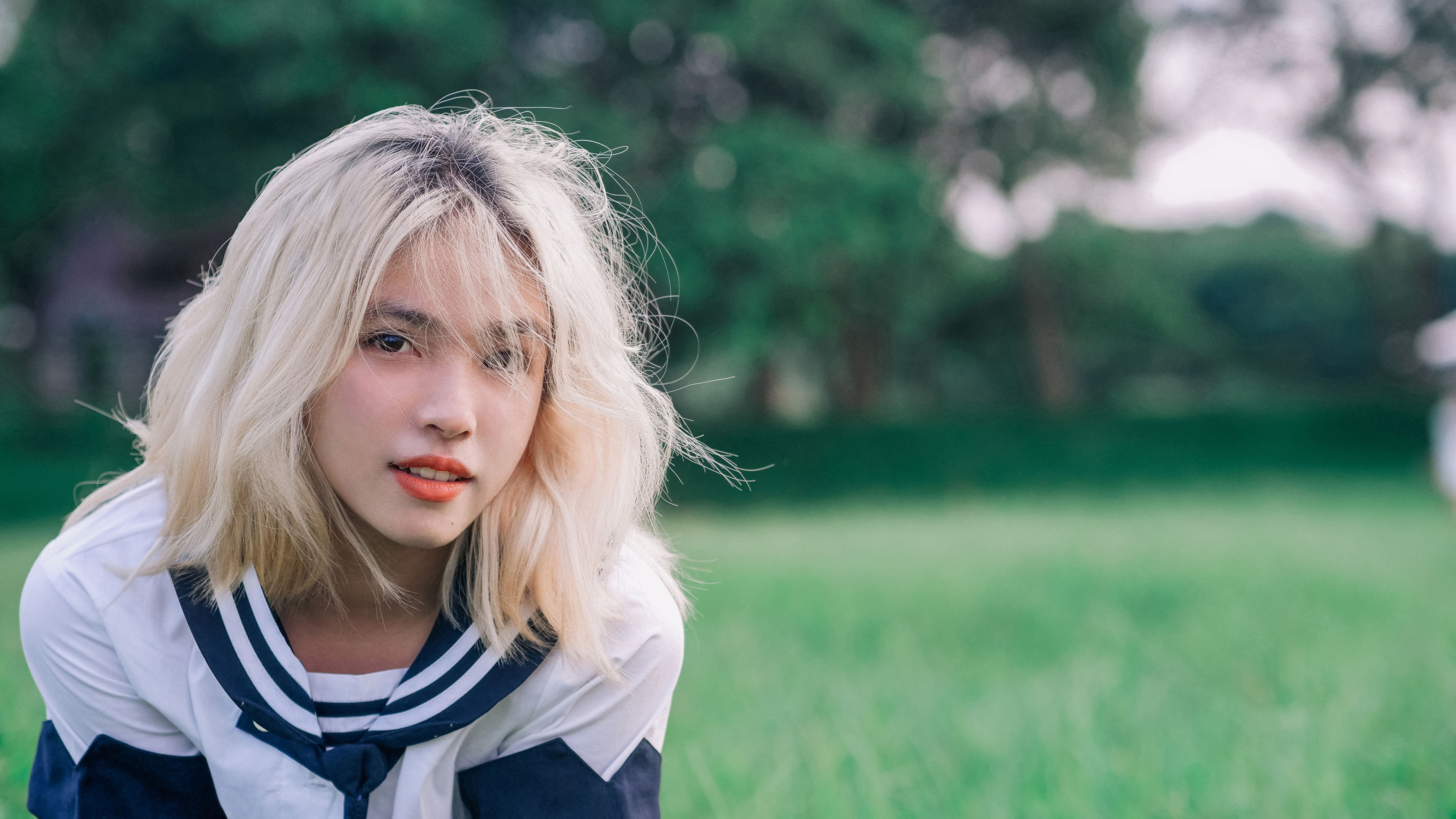 A young woman with blonde hair poses outdoors on a summer day.