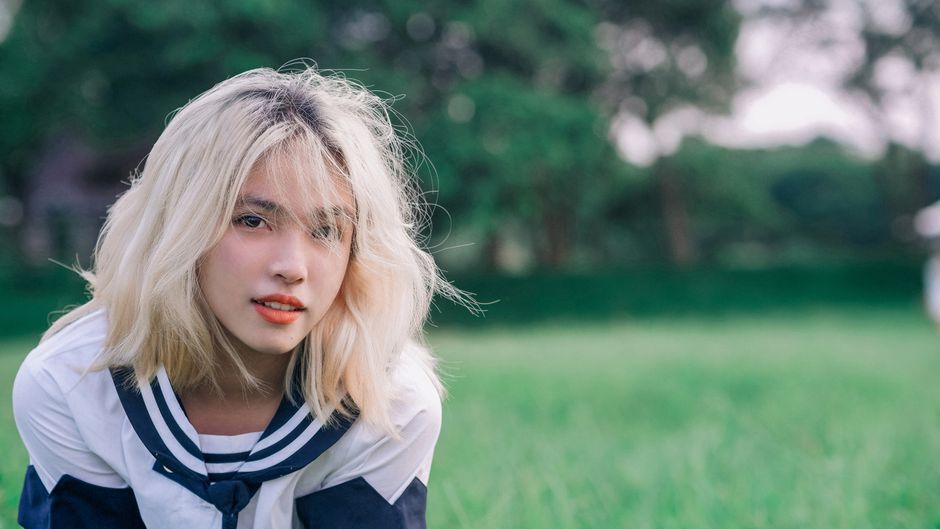 A young woman with blonde hair poses outdoors on a summer day.