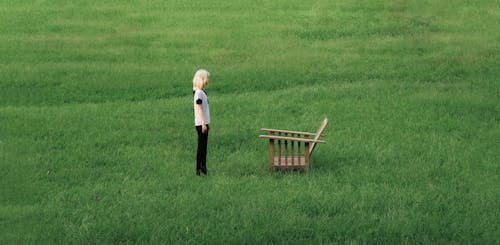 Woman Standing Near Wooden Chair on Green Grass Field 