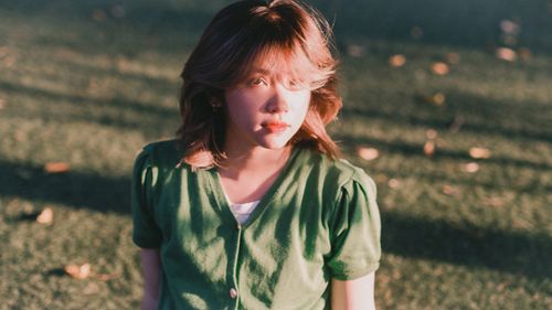 Free A woman with wavy hair in a green outfit bathed in warm sunlight outdoors. Stock Photo