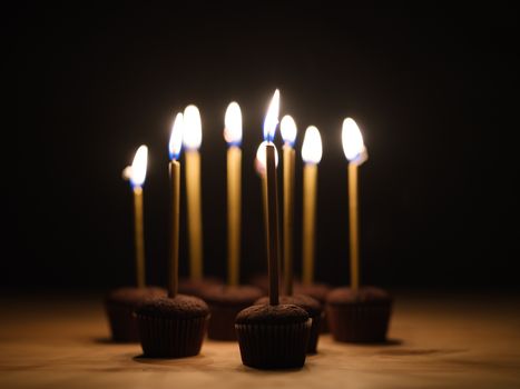 Chocolate cupcakes with flaming candles against a dark backdrop, ideal for celebration themes.