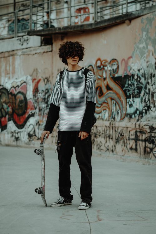 Free Young man with skateboard standing in an urban skatepark with graffiti walls. Stock Photo