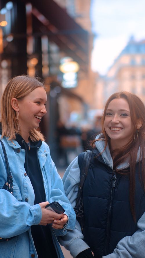 Free Two young women in casual jackets smiling and enjoying a stroll on a city street. Stock Photo