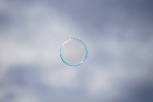 A solitary soap bubble gently floats against a soft, cloudy sky, epitomizing fragility and whimsy.