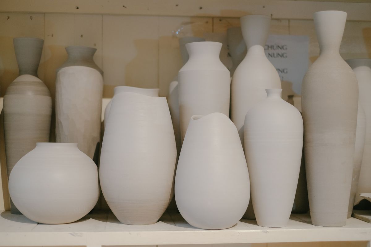 Rows of matte white ceramic vases in different shapes on a wooden shelf