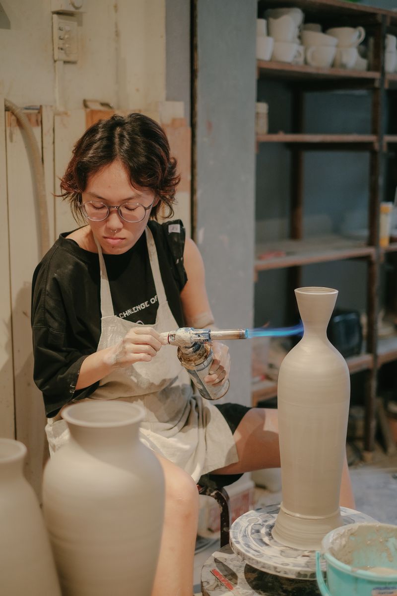 A potter in an apron using a small torch on a tall clay vase