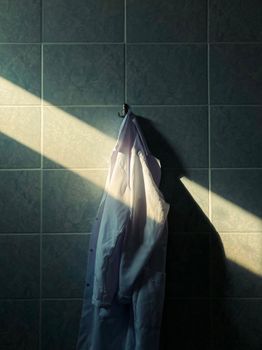 A single coat hanging on a tiled wall, illuminated by a beam of sunlight creating a serene atmosphere.