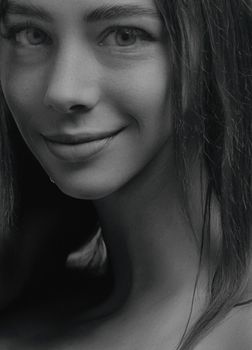 Close-up black and white portrait of a smiling woman with soft lighting.