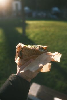 Hand holding a freshly made sandwich wrapped in paper in a sunny Dublin park, showcasing casual outdoor dining.