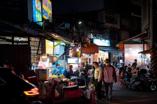 Lively night market scene with food stalls and people in a bustling urban setting.