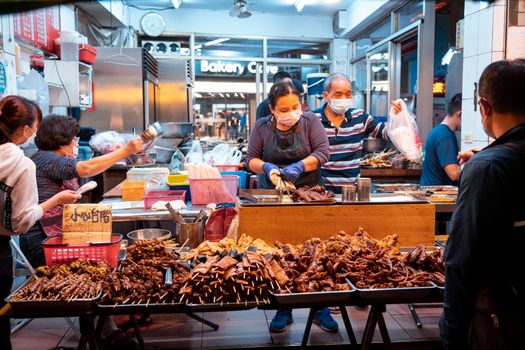 Night market scene with vendors serving diverse skewers and food to customers.