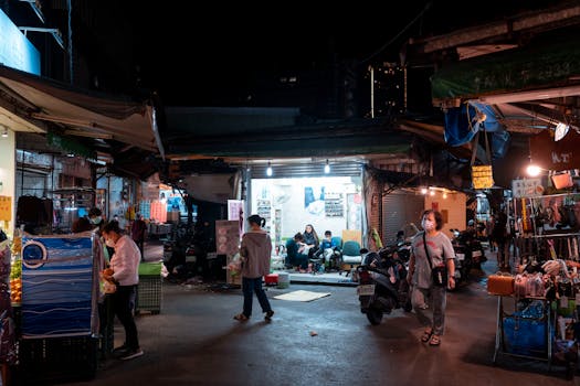 Bustling night market with people shopping at illuminated stalls and stores.