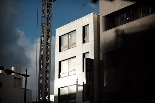 Sunlit modern building with construction crane against a cloudy sky.