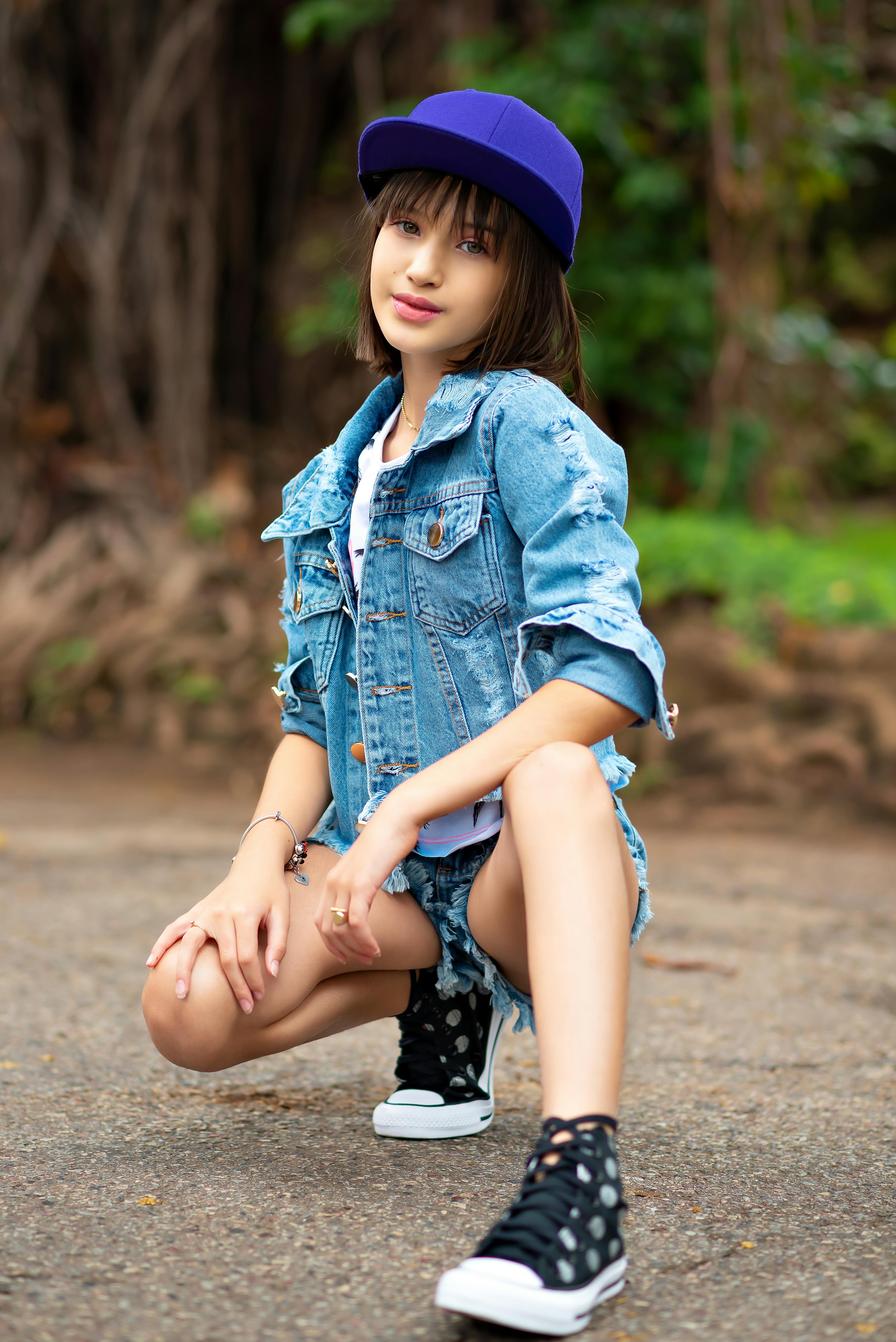 Teen girl posing in stylish denim outfit with cap in an outdoor setting.