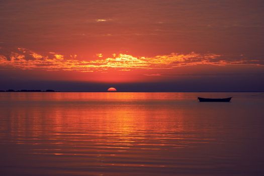 A peaceful sunset scene with a boat on a tranquil sea. Perfect for serene backgrounds.