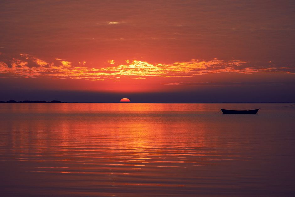 A peaceful sunset scene with a boat on a tranquil sea. Perfect for serene backgrounds.