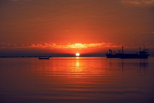 Free Silhouette of boats against a vibrant sunset over a calm sea. Stock Photo