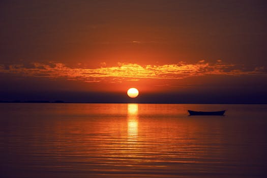 A serene sunset over a calm ocean with a silhouetted boat, creating a tranquil atmosphere.